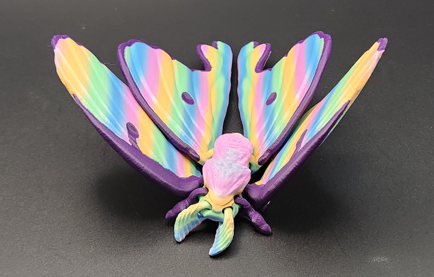 Colorful 3D printed luminous moth figurine with rainbow wings displayed on a black surface