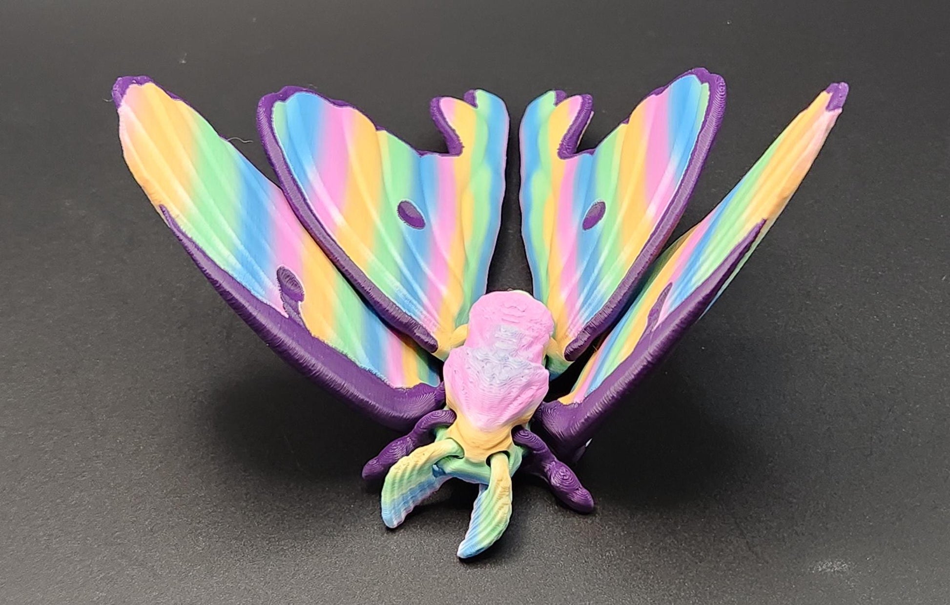 Colorful 3D printed luminous moth figurine with rainbow wings displayed on a black surface