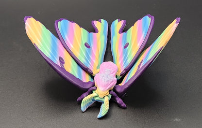 Colorful 3D printed luminous moth figurine with rainbow wings displayed on a black surface