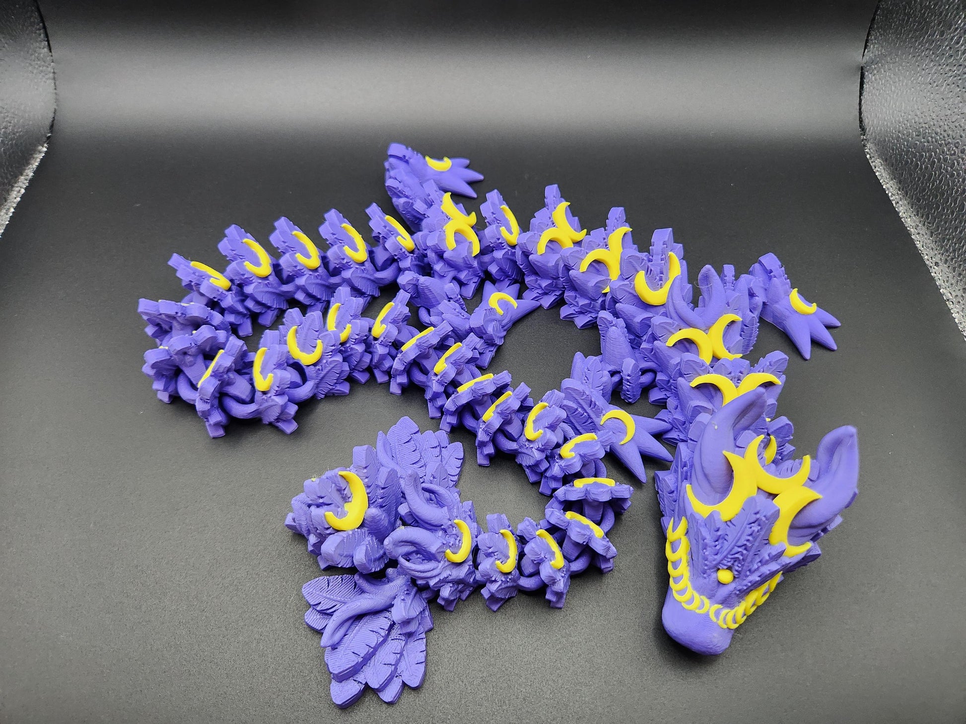 Purple and yellow 3D printed lunar dragon figure with intricate details displayed on a black surface