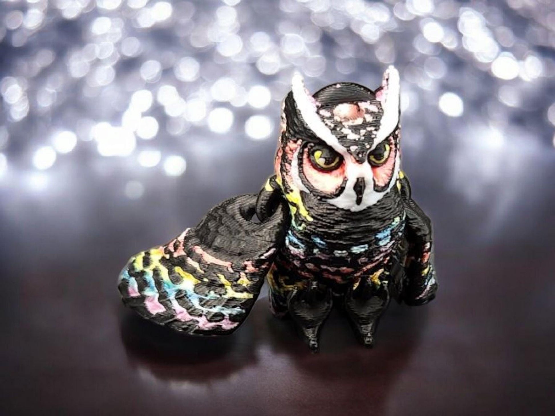 Colorful 3D printed owl keychain with detailed feathers and large eyes on a reflective surface