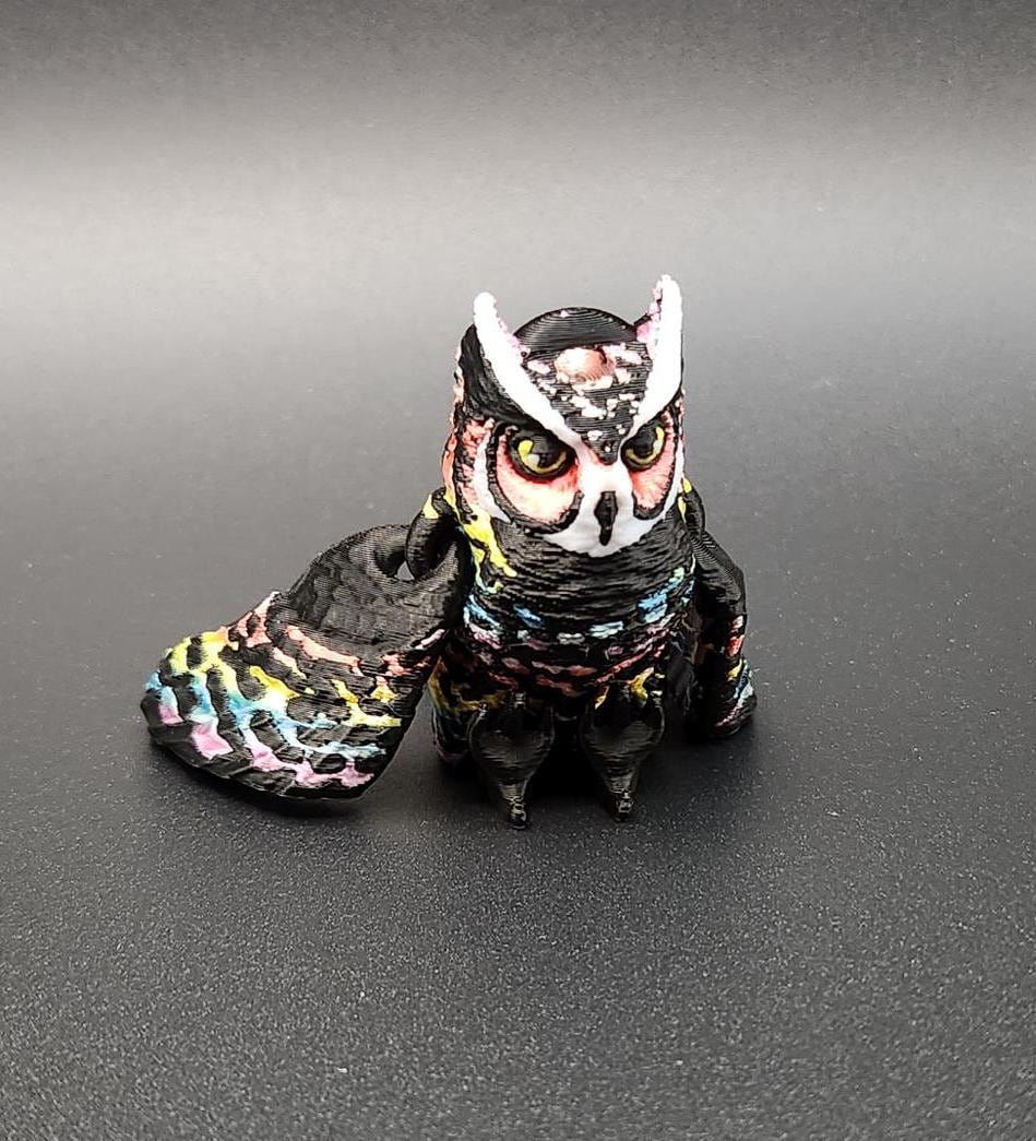 Colorful detailed 3D printed owl keychain with large eyes and vibrant feather design on black background
