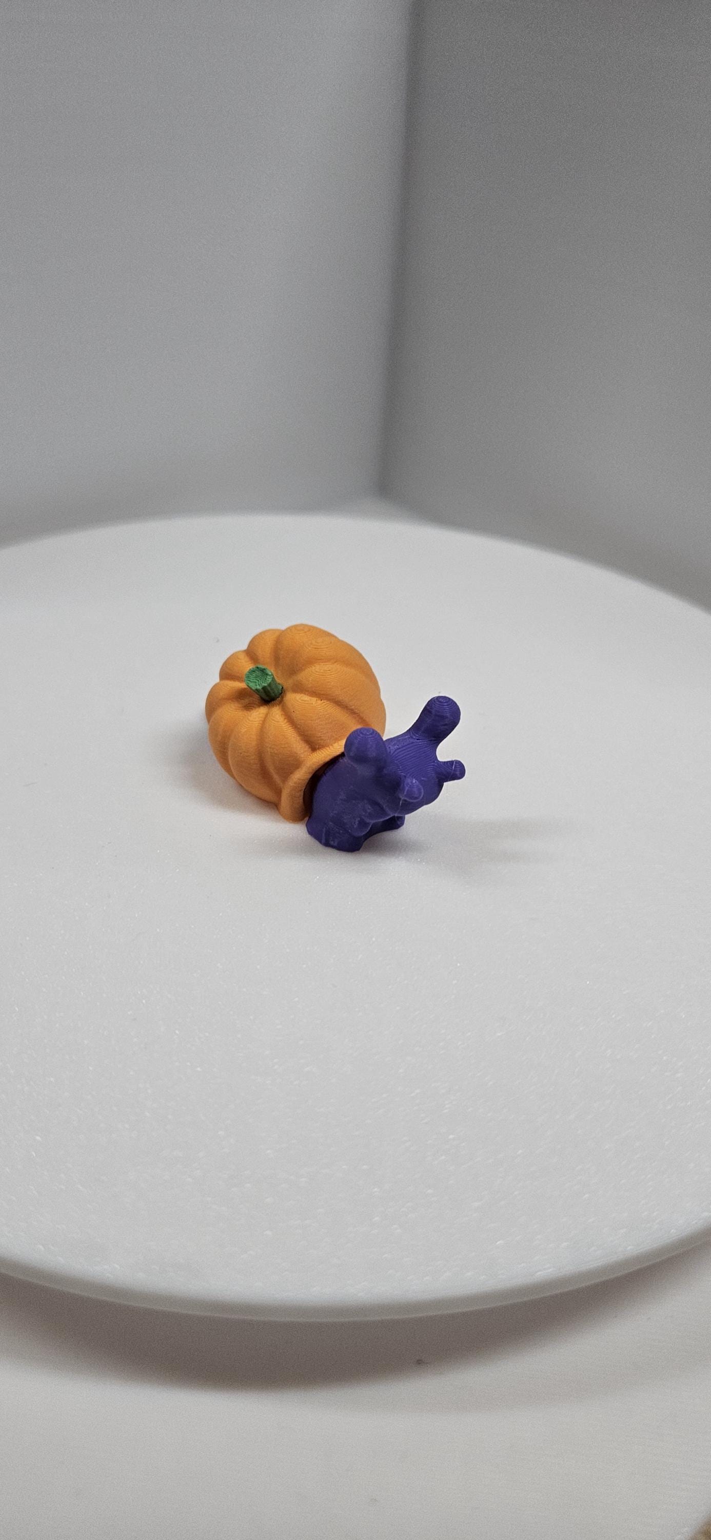 3D printed pumpkin snail figurine with an orange pumpkin shell and a purple snail body on a white surface