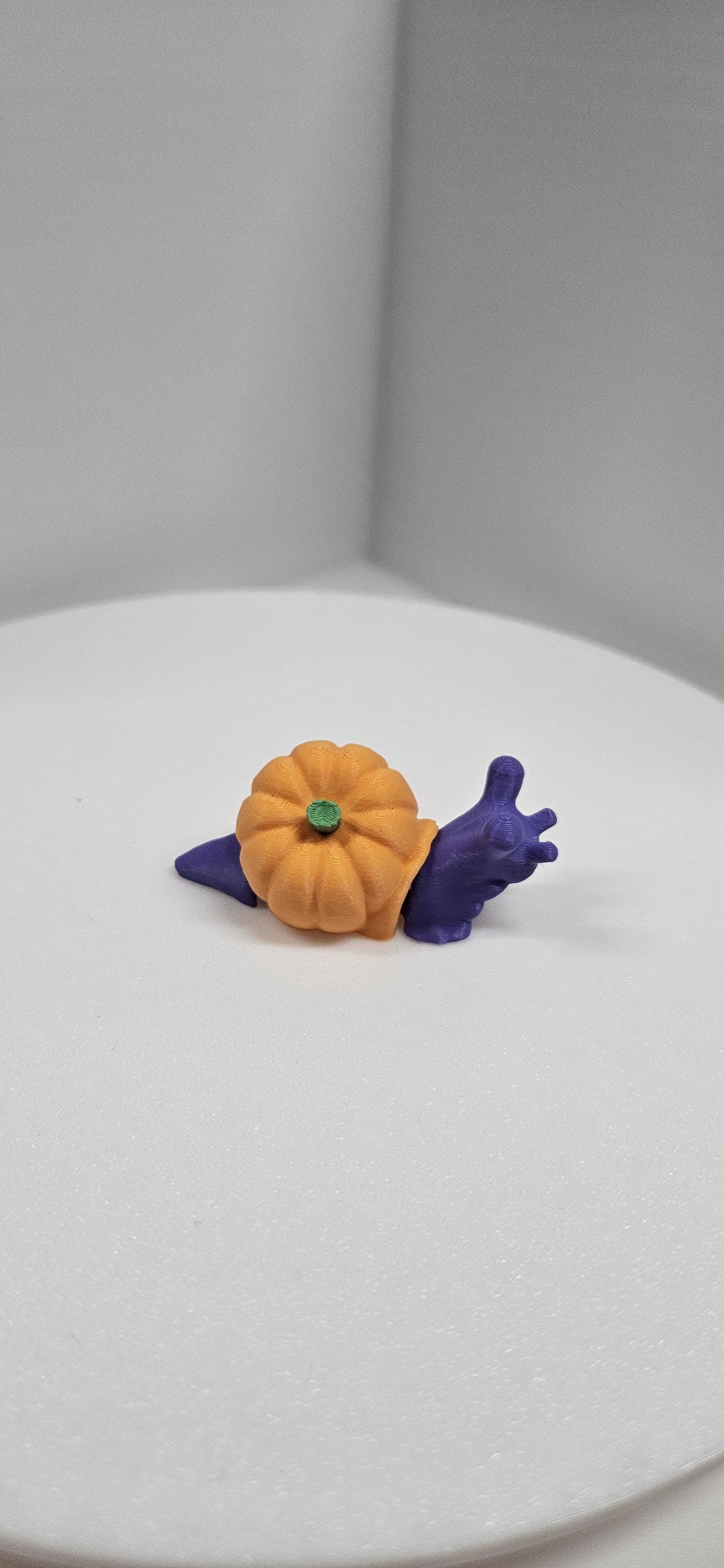 3D printed pumpkin snail with an orange pumpkin shell and purple snail body on white surface