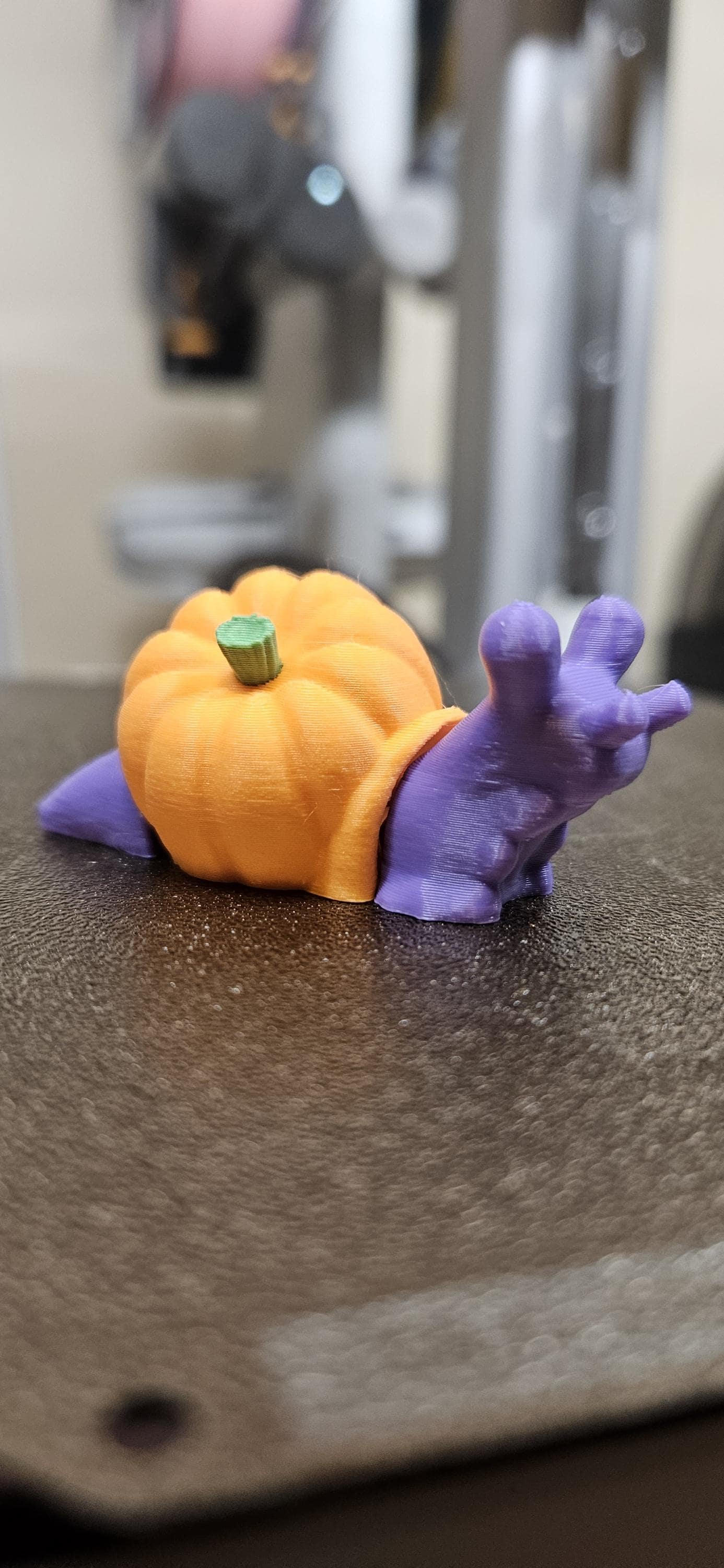 Colorful 3D printed pumpkin snail with an orange pumpkin shell and purple body on a black surface