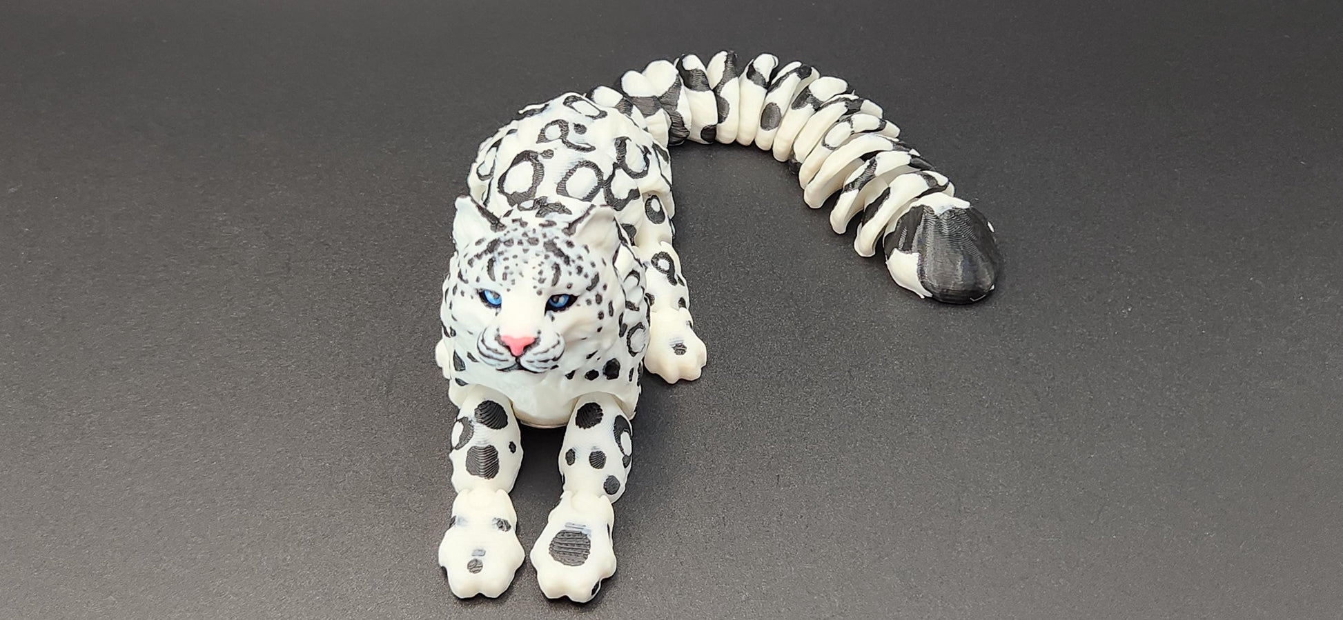 3D printed snow leopard figurine in white with black spots lying on gray surface from Etsy