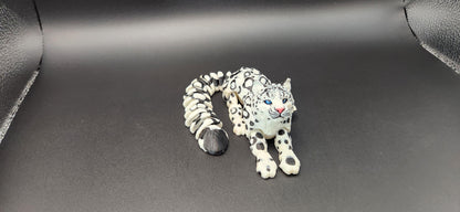 3D printed snow leopard figurine with detailed black spots and blue eyes on a black surface