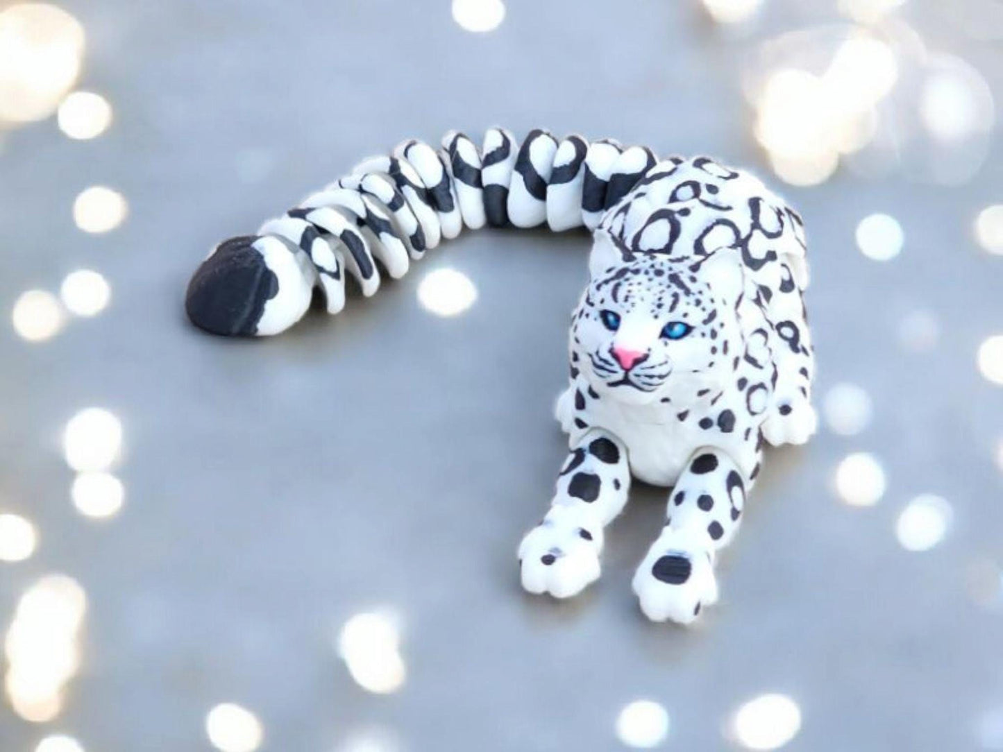 3D printed snow leopard figurine in white with black spots and blue eyes on a gray surface