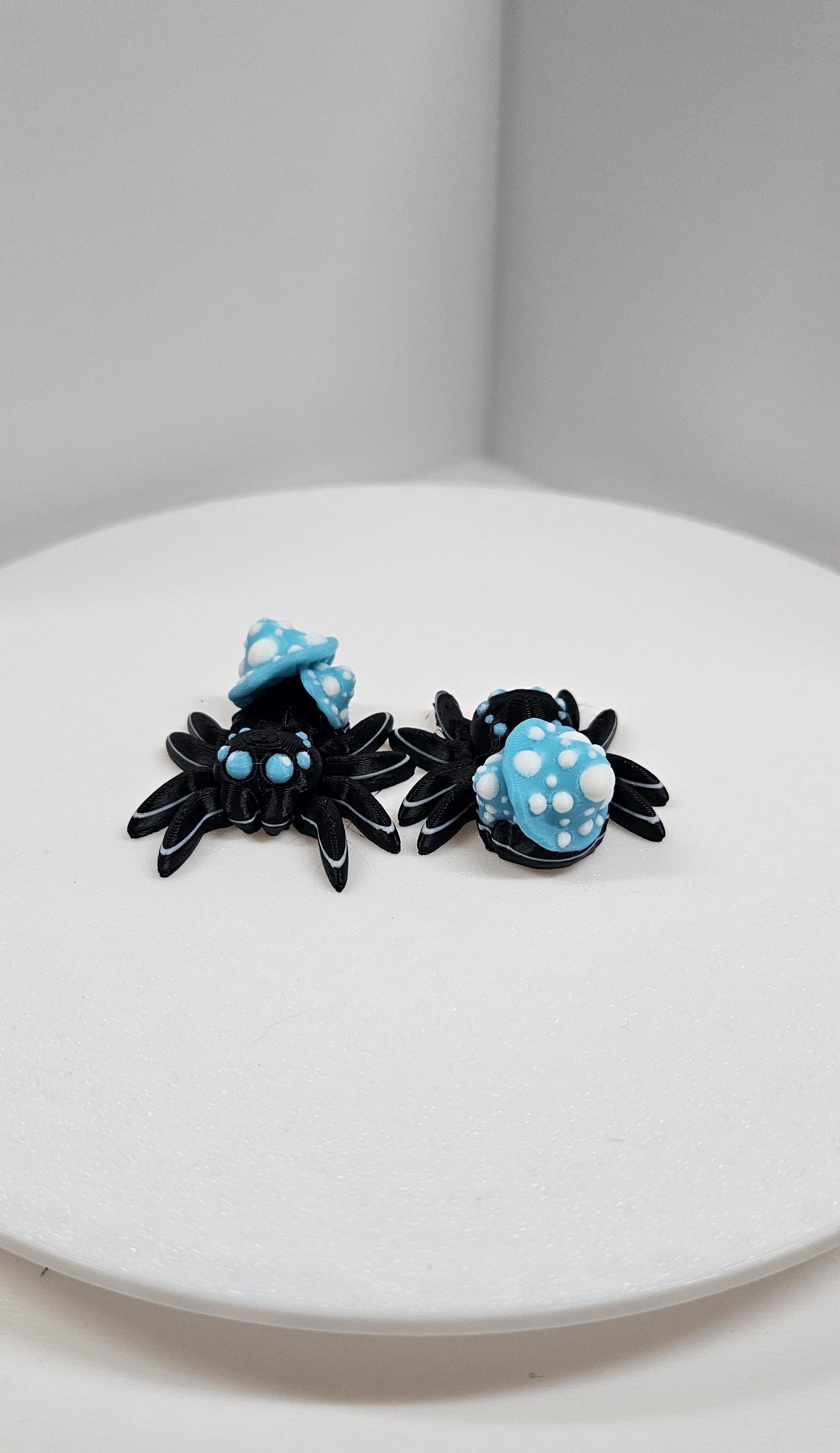 Two black and blue 3D printed spider fidget toys with polka dot designs on a white surface