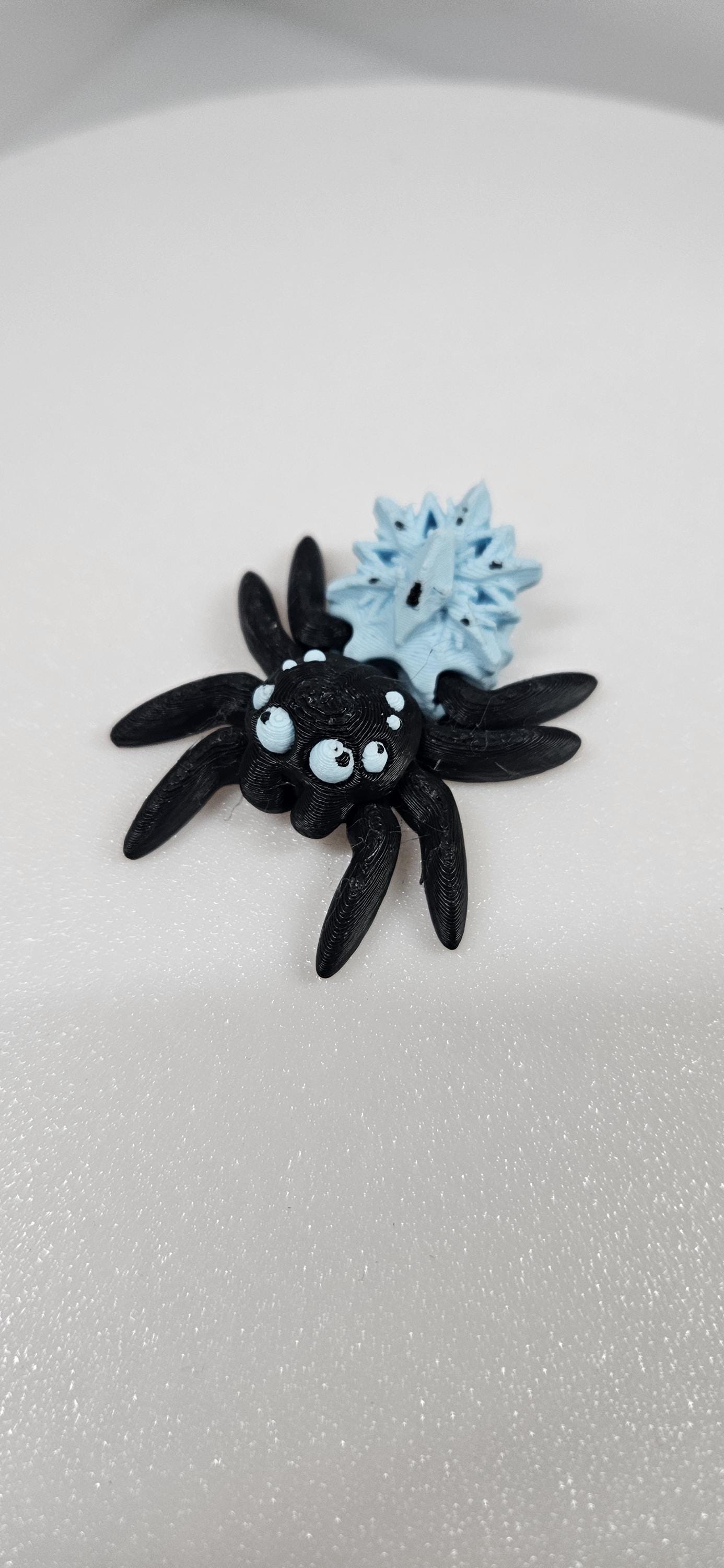 Black and blue 3D printed spider fidget toy with googly eyes on a white surface