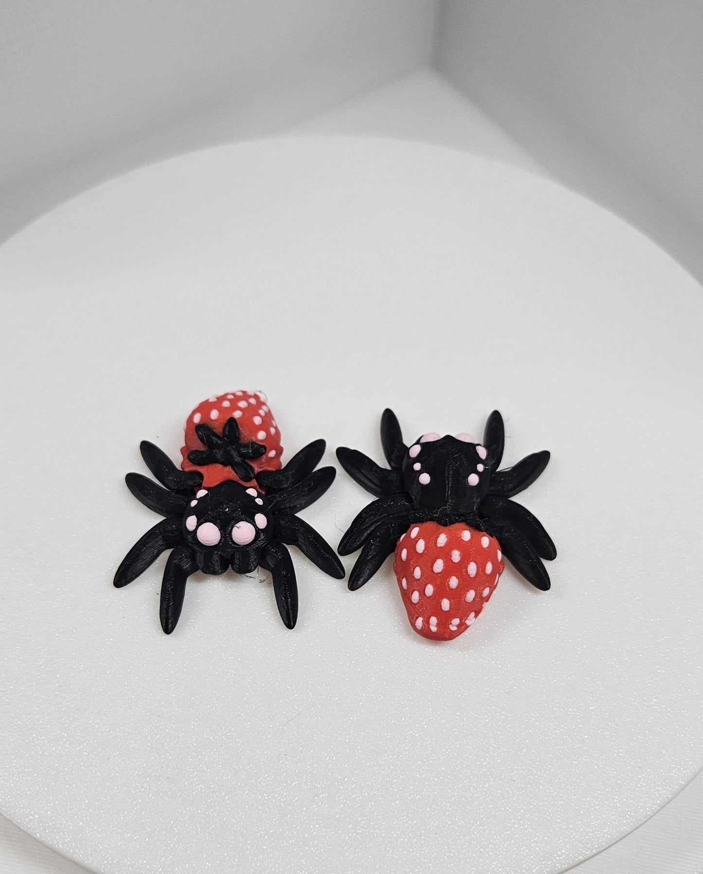 Two 3D printed spider fidget toys in black and red with white dots displayed on a white surface