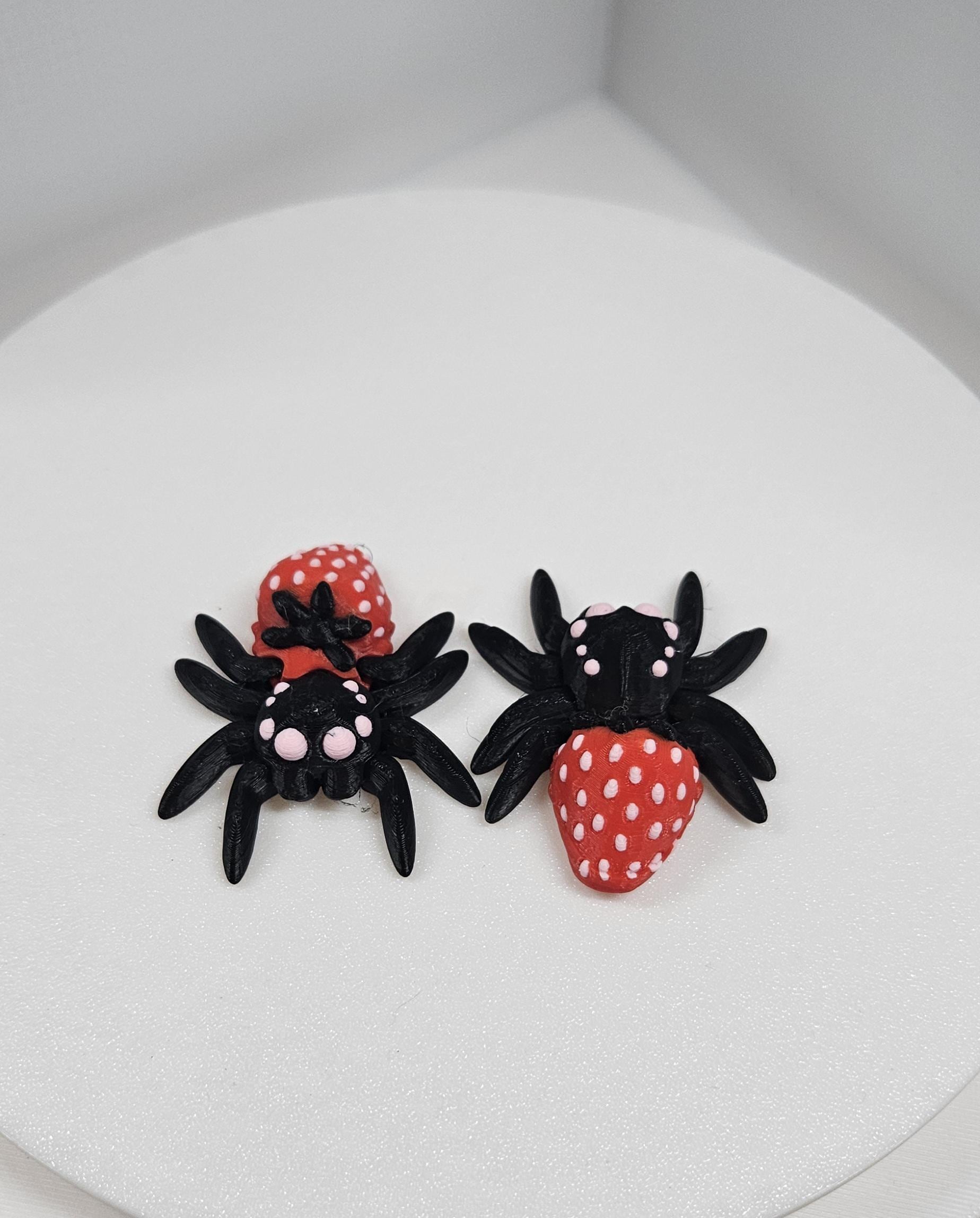 Two 3D printed spider fidget toys in black and red with white dots displayed on a white surface