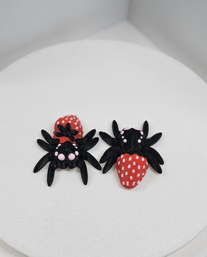 Two 3D printed spider fidget toys in black and red with white dots displayed on a white surface