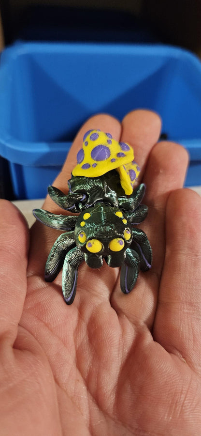 Close-up of a 3D printed spider fidget toy in black with yellow and purple mushroom details held in a hand