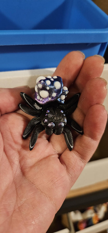 Hand holding a black and purple 3D printed spider fidget toy with textured details