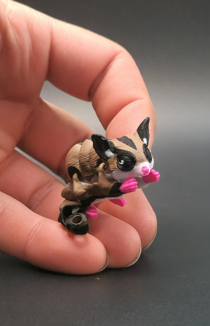 Hand holding a detailed 3D printed sugar glider keychain with pink paws and black eyes