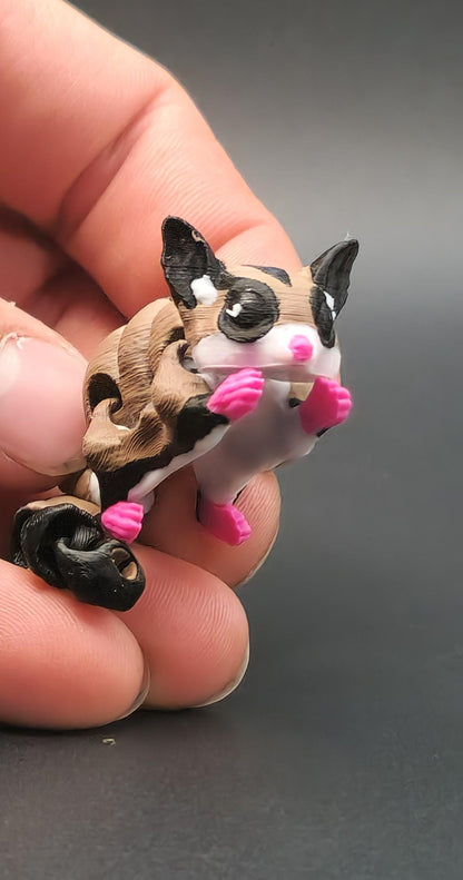 Hand holding a 3D printed sugar glider keychain with detailed pink paws and black striped design