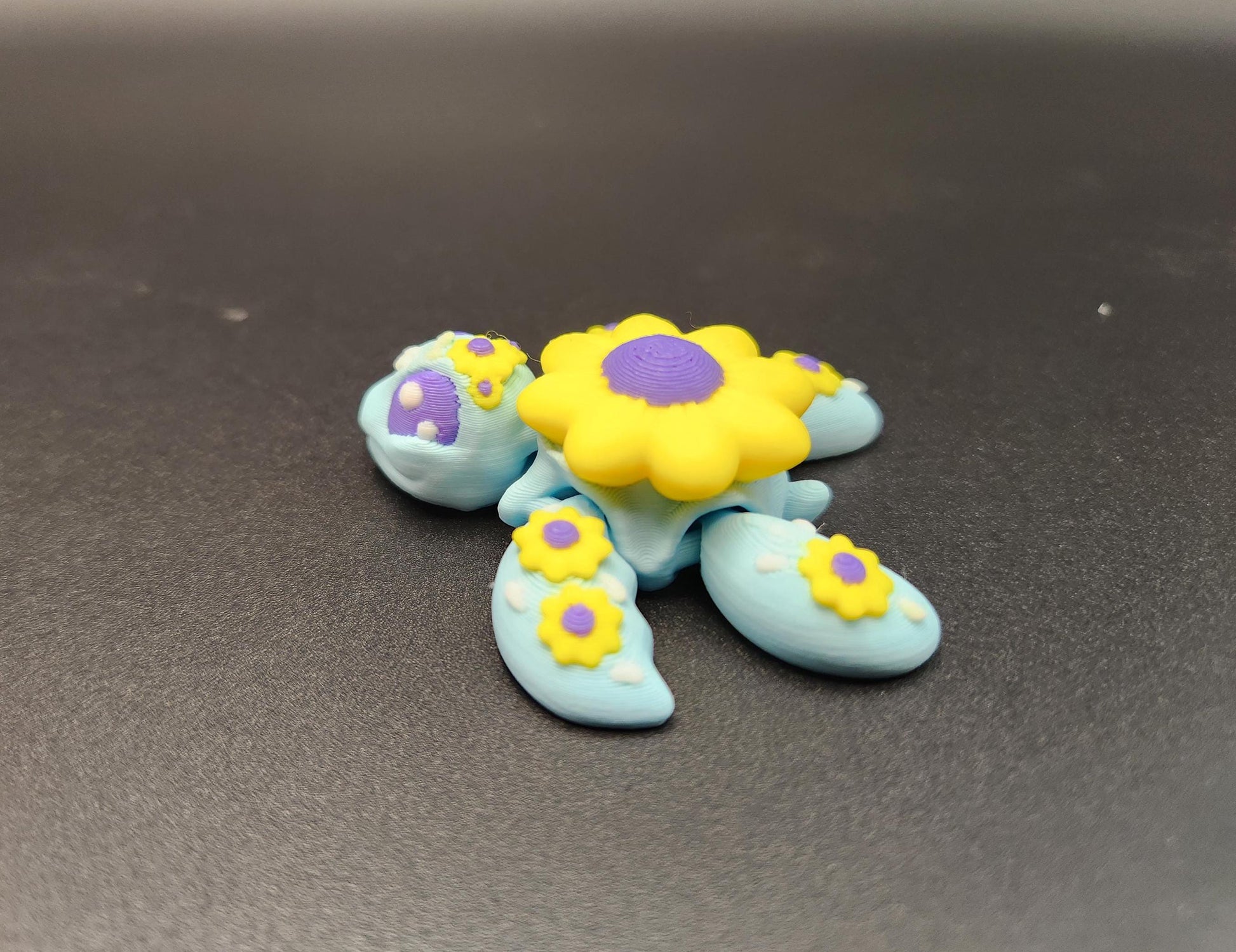 3D printed sunflower turtle in blue with yellow and purple flower designs on a black surface