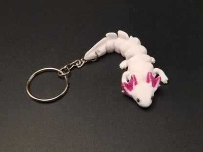 White articulated axolotl keychain with pink gills and metal ring on black background