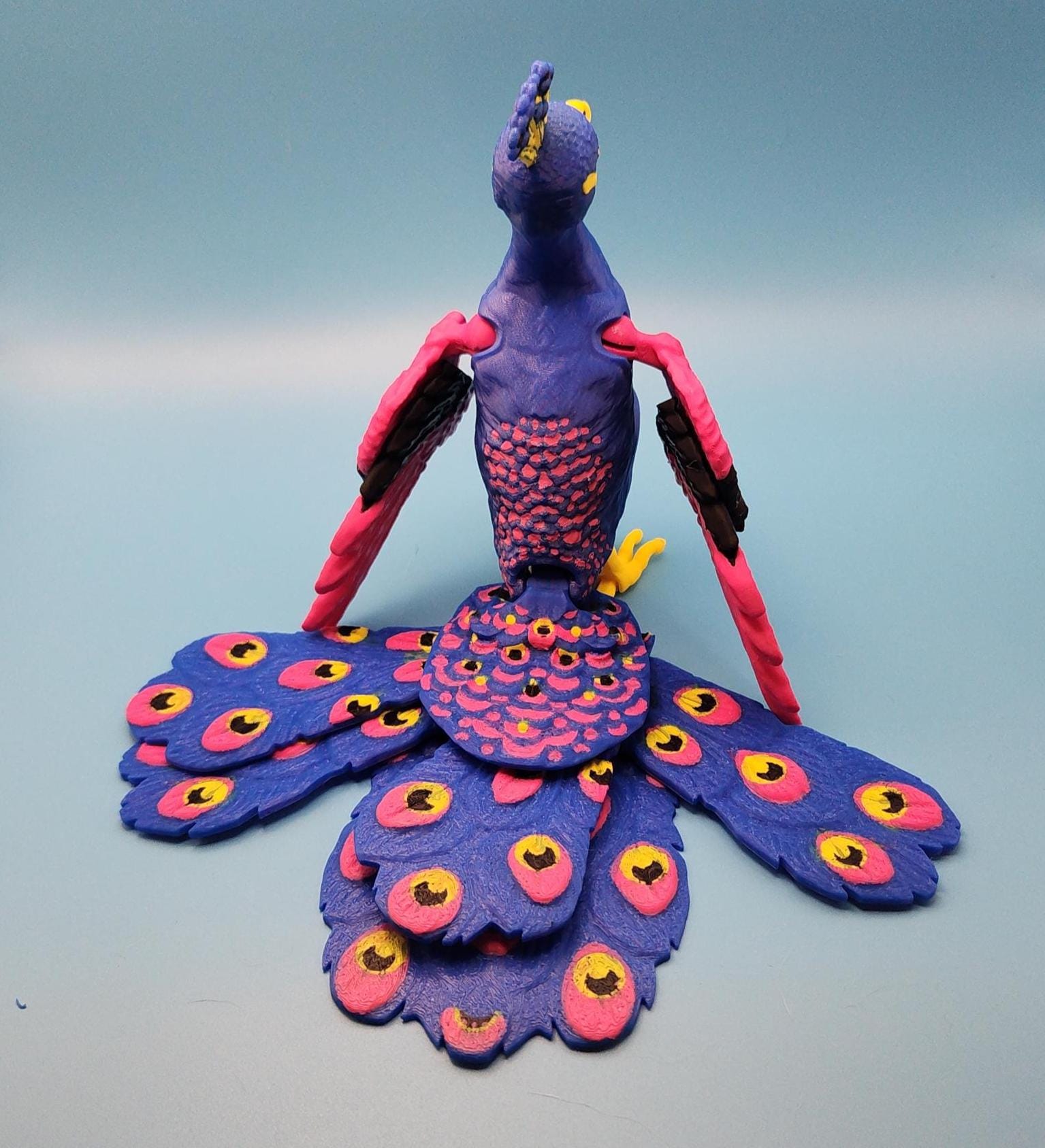 Colorful handcrafted articulated bird desk decor in vibrant purple, pink, and yellow colors with movable wings and tail feathers
