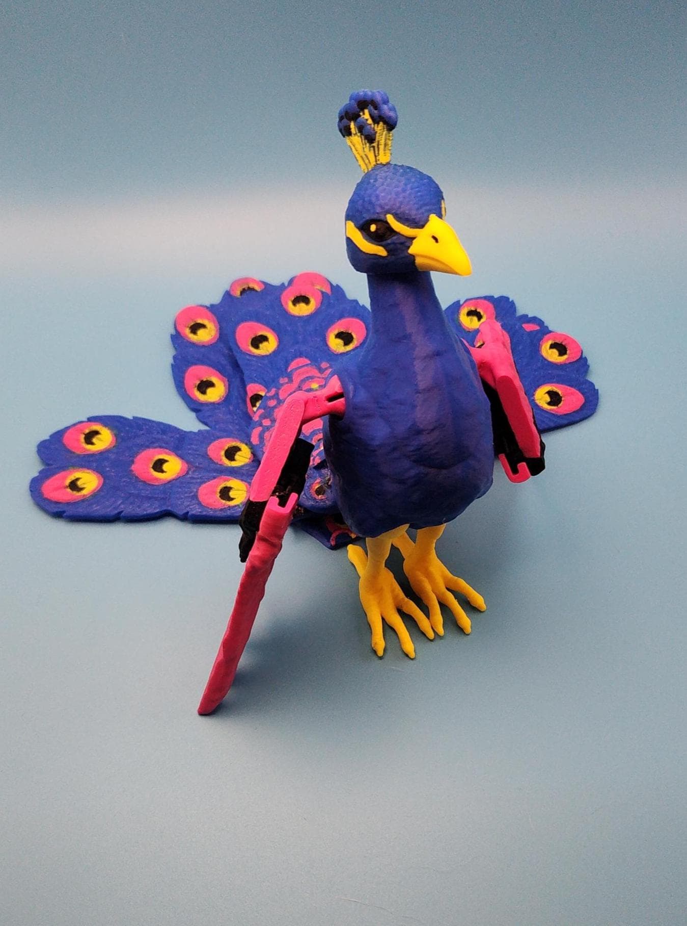 Colorful articulated bird desk decor featuring a blue and pink peacock with movable wings and tail feathers