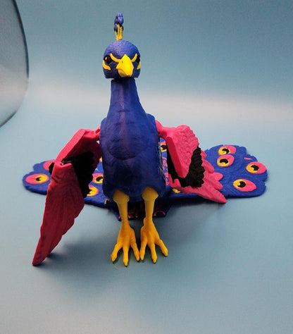 Blue and pink articulated bird desk decor resembling a colorful peacock with movable wings