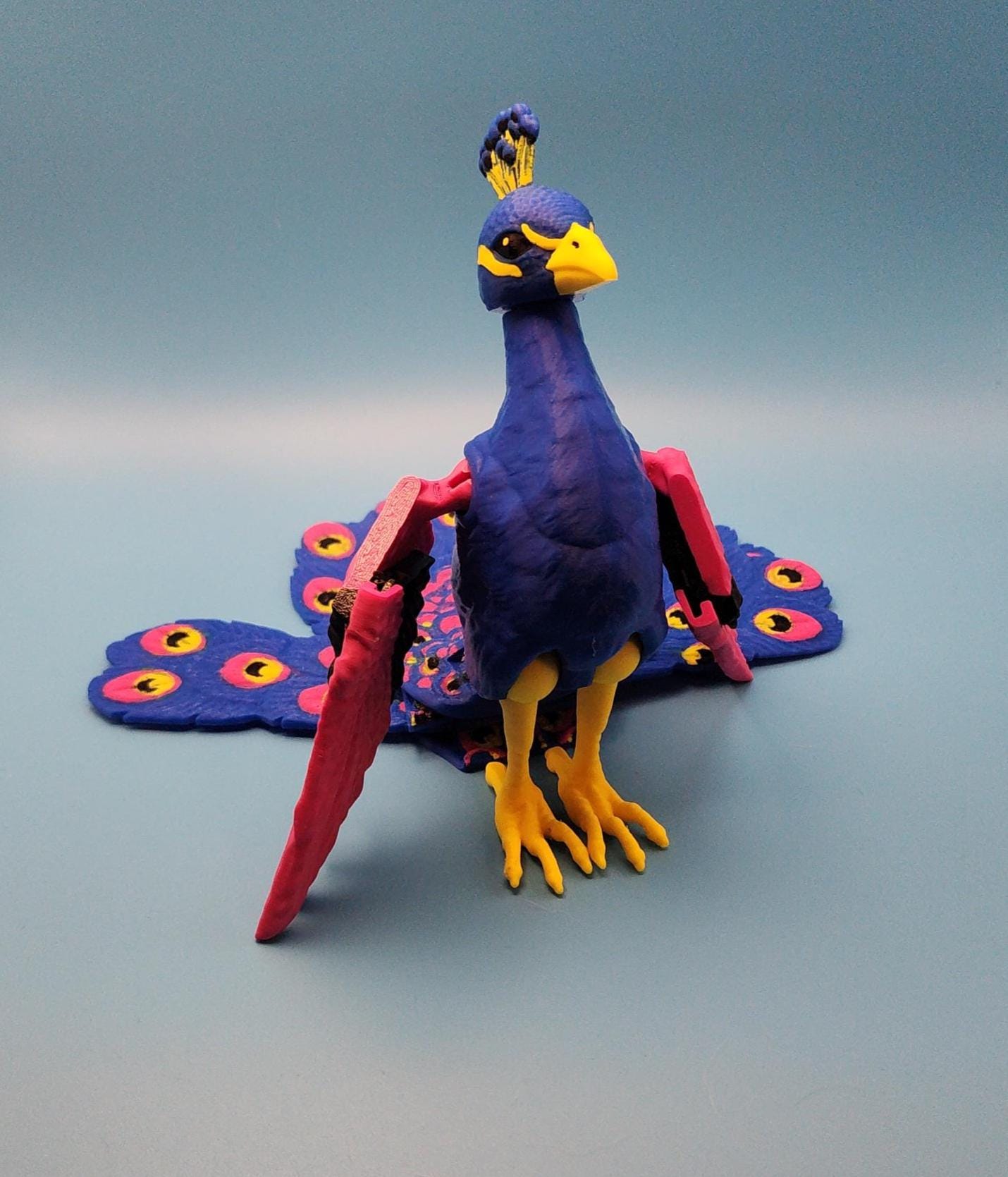 Colorful articulated bird desk decor resembling a peacock with blue, yellow, and pink details