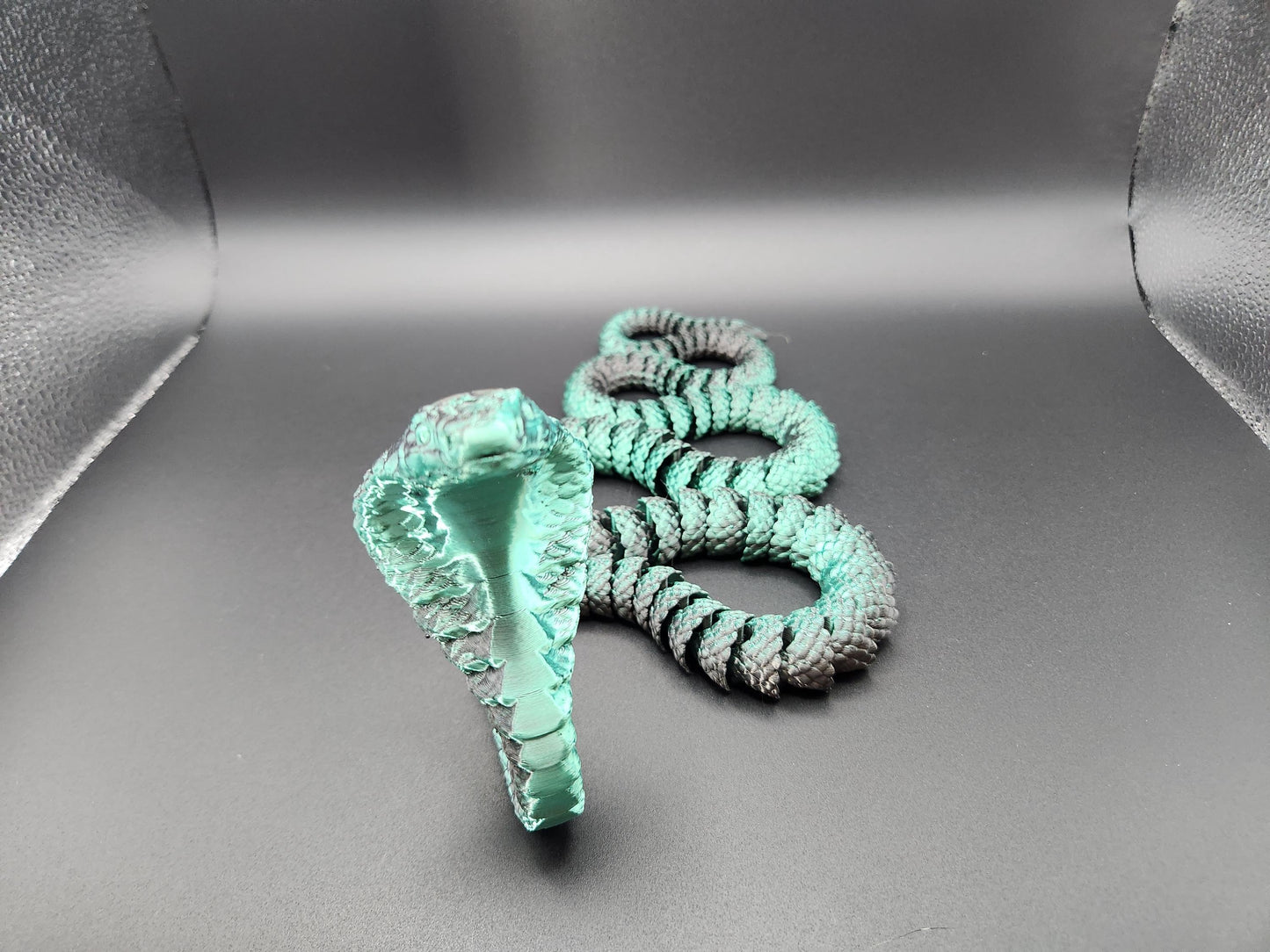 Handcrafted articulated king cobra toy in turquoise and black displayed on gray background