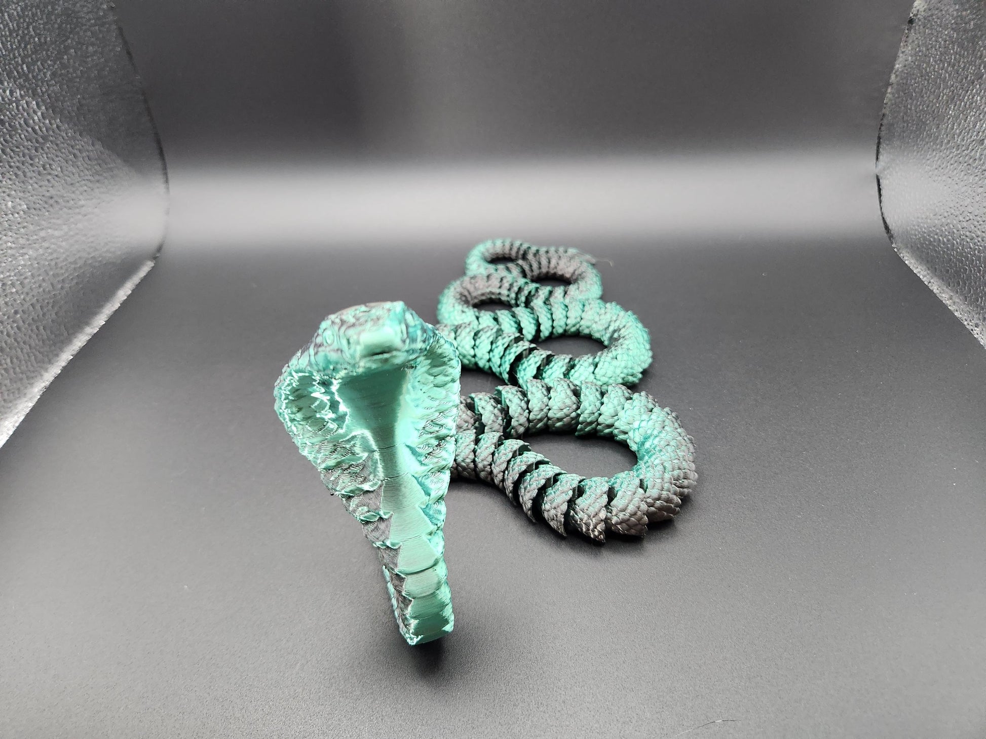 Handcrafted articulated king cobra toy in turquoise and black displayed on gray background