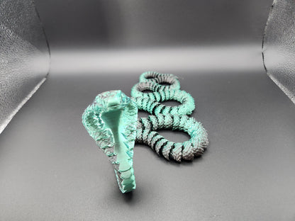 Handcrafted articulated king cobra toy in turquoise and black displayed on gray background