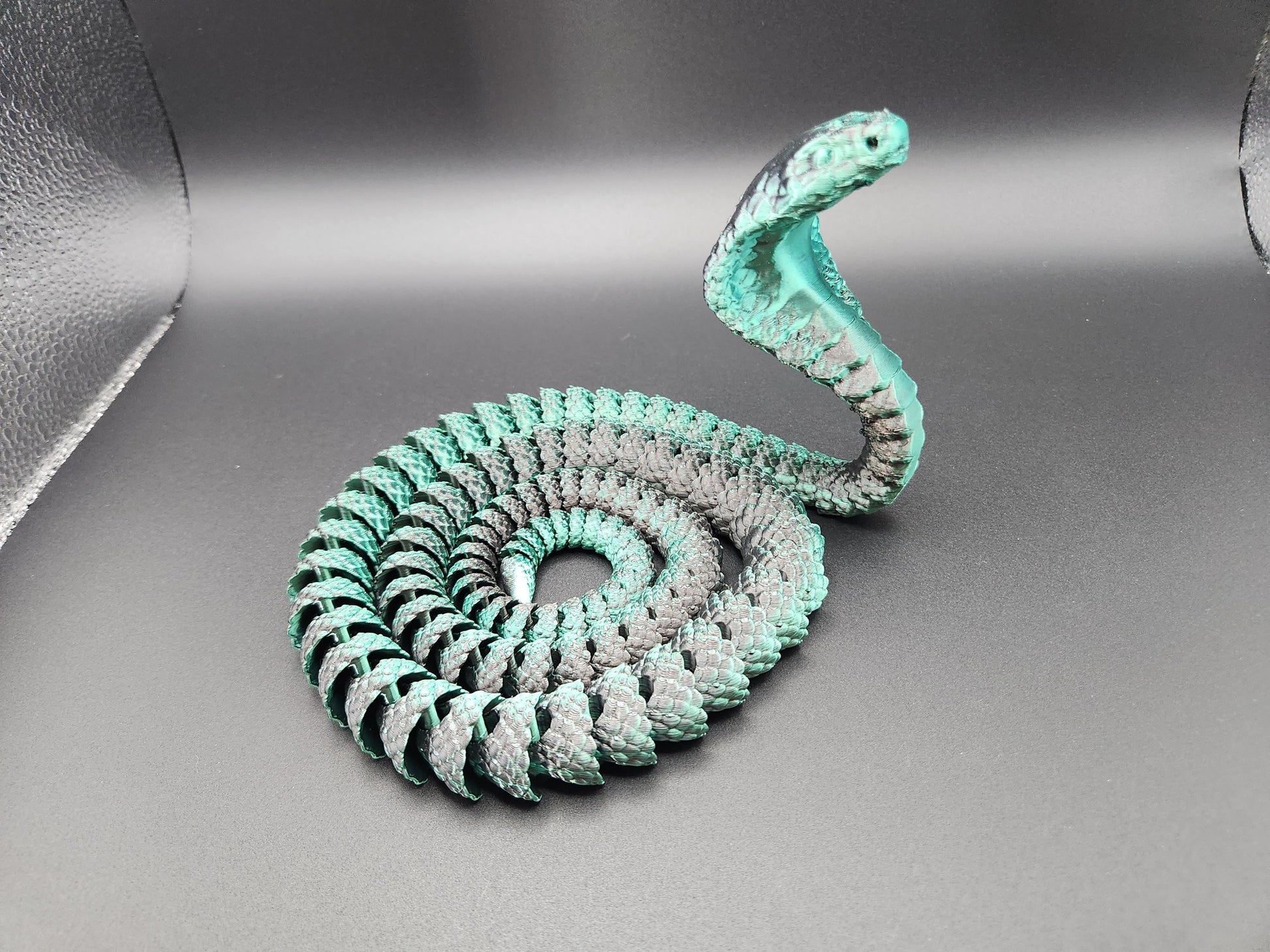 Articulated king cobra toy in coiled position with detailed scales and raised hood on gray background