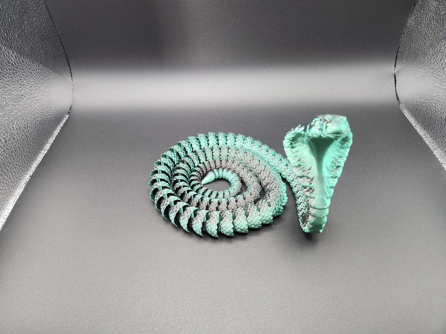 Green articulated king cobra toy coiled with raised hood on a dark background