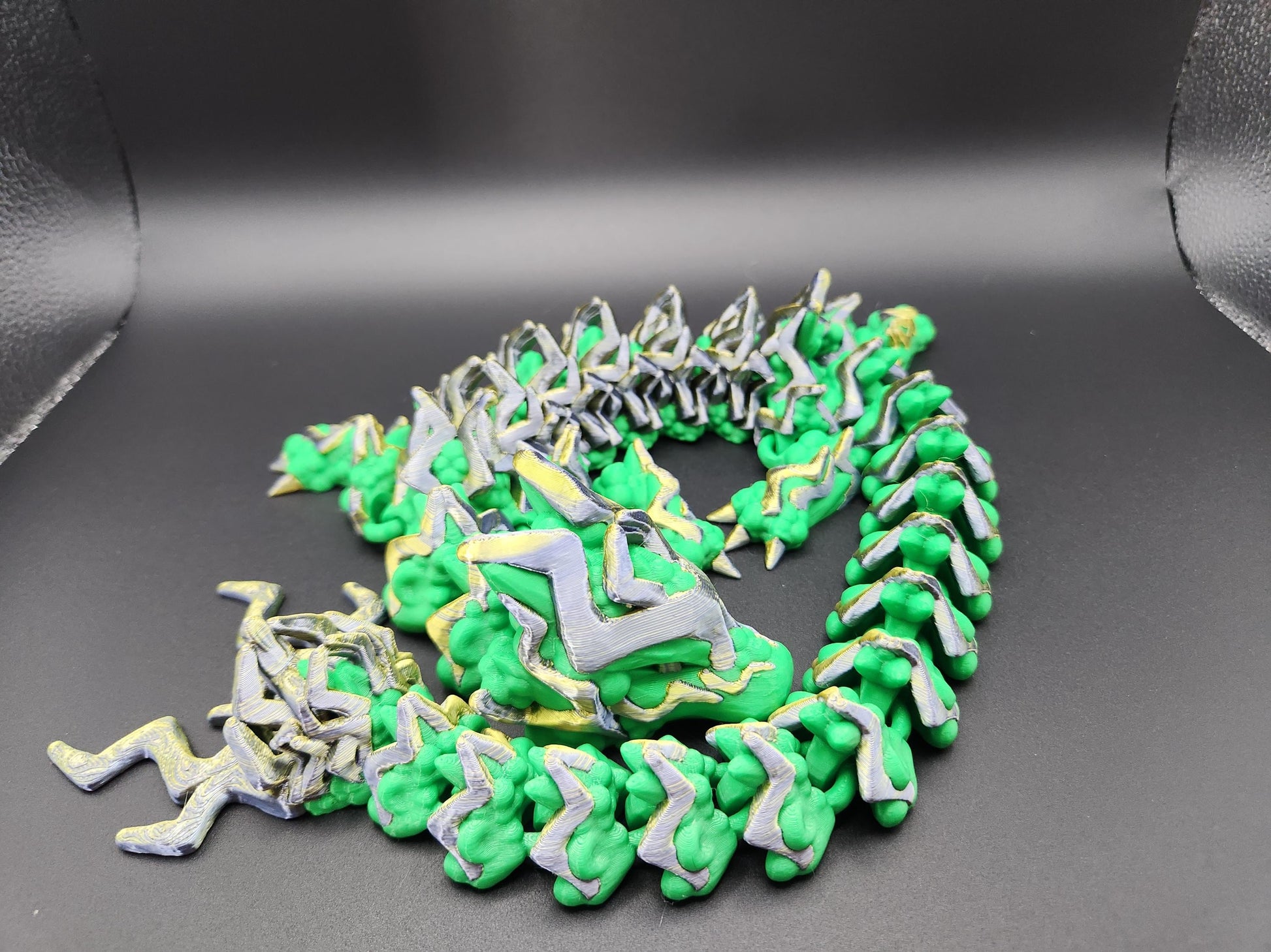 Green and silver articulated storm dragon figurine with detailed segmented body on black background