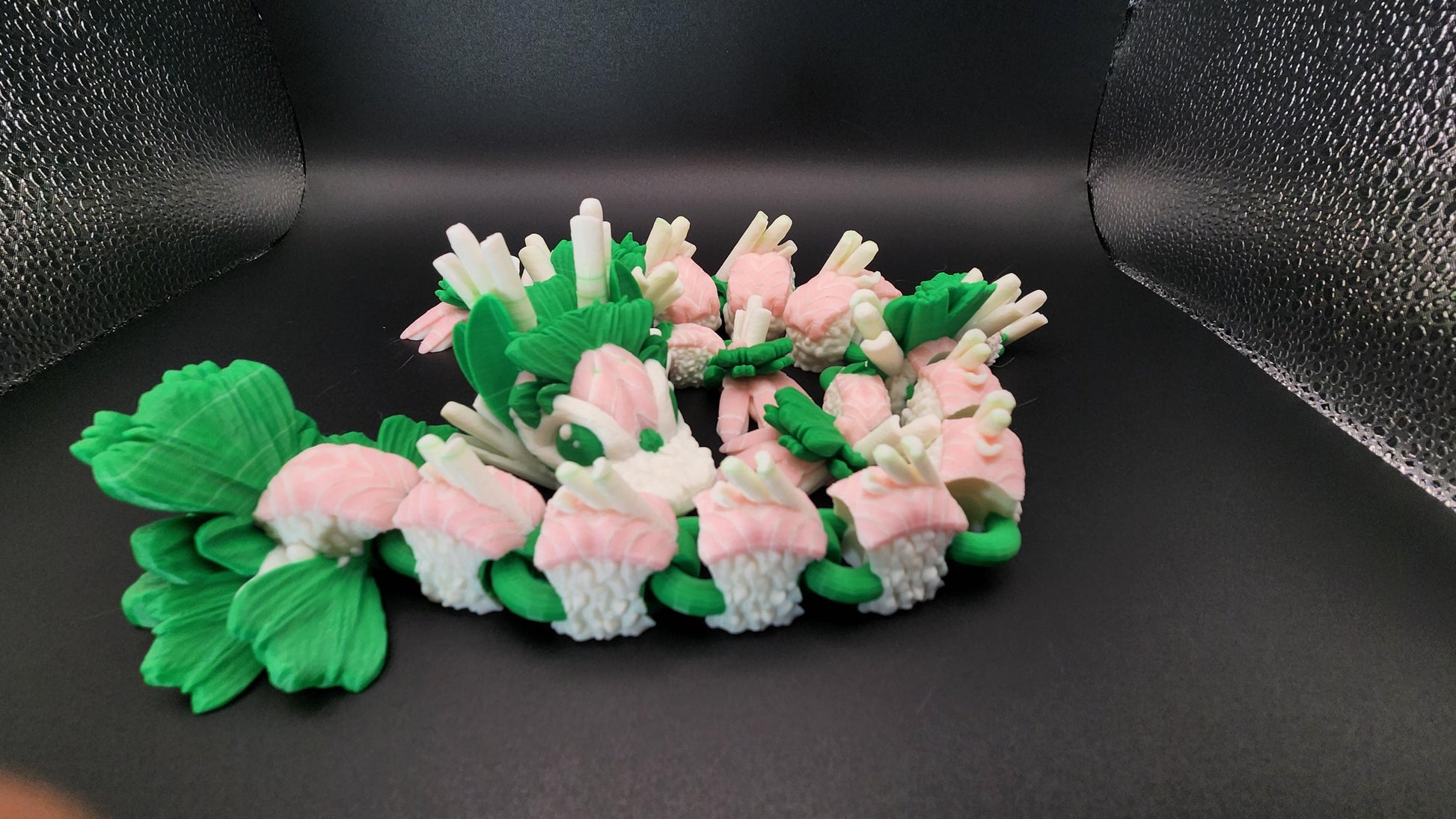 Articulated sushi dragon figurine made of green and pink sushi pieces with detailed tail and claws