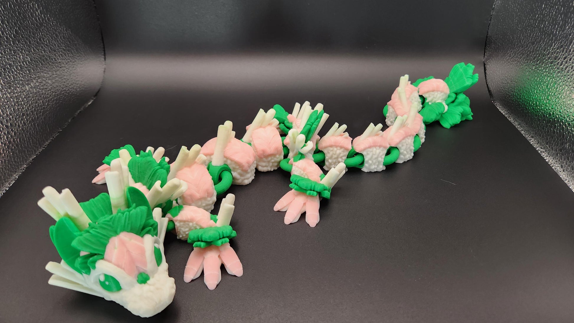 Green and pink articulated sushi dragon figurine with multiple segments on a black background