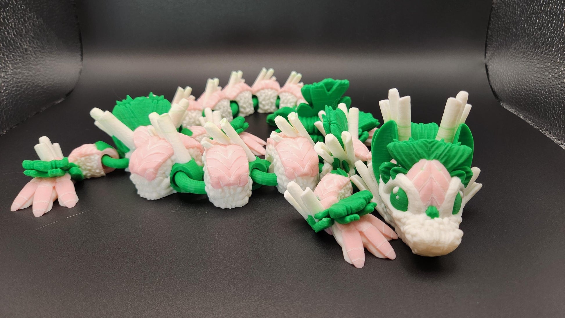 Articulated sushi dragon figurine in pink white and green displayed on black background