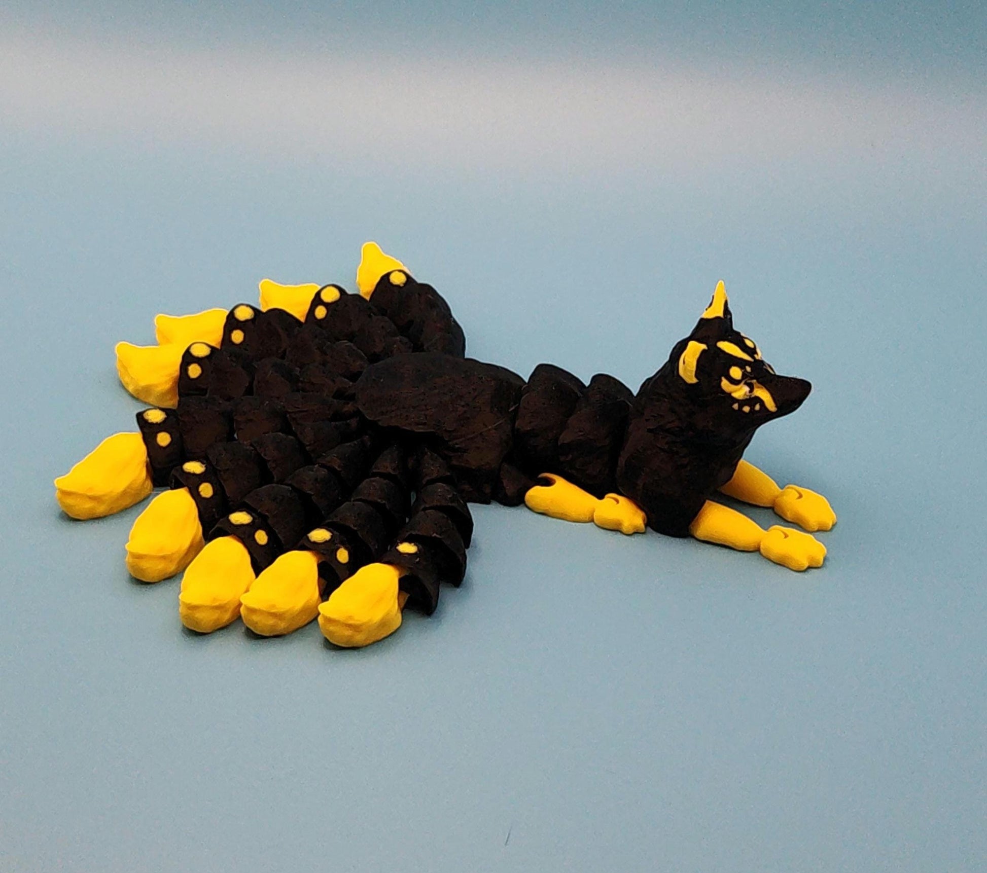 Handcrafted Japanese kitsune figurine 9-tailed fox mythical creature in black and yellow on blue background