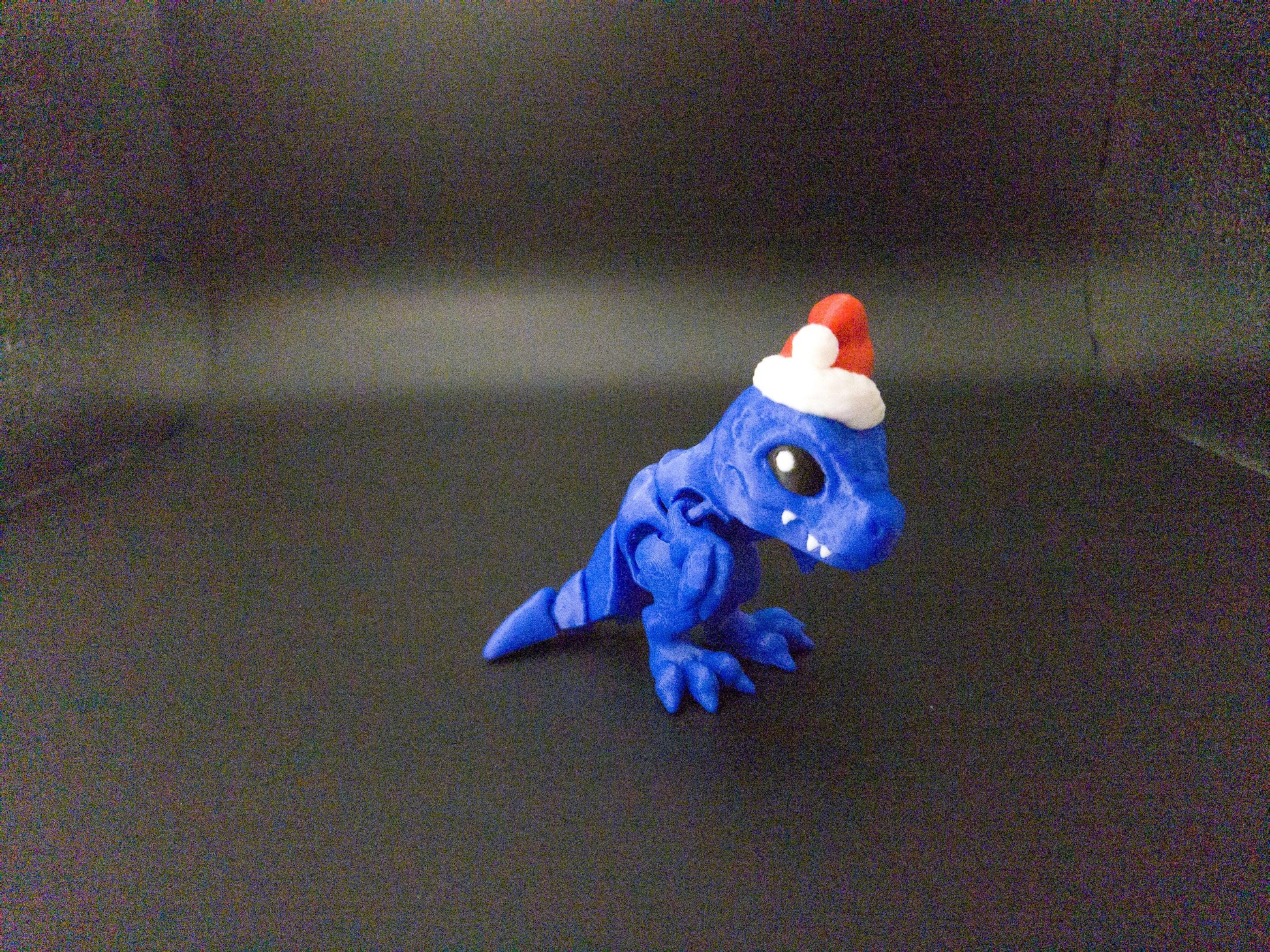 Blue Christmas Santa T-Rex figurine wearing a red and white Santa hat on black background