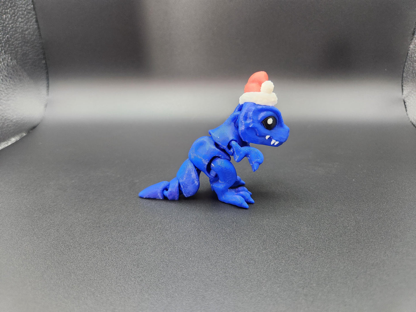 Blue Christmas Santa T-Rex figurine wearing a red and white Santa hat on gray background