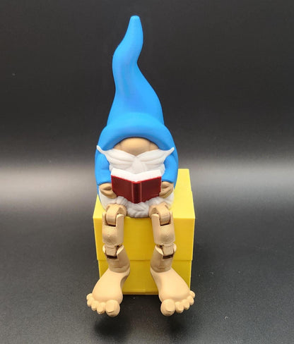 Blue hat gnome sitting on yellow box holding a red book book lover gnome ornament shelf buddy