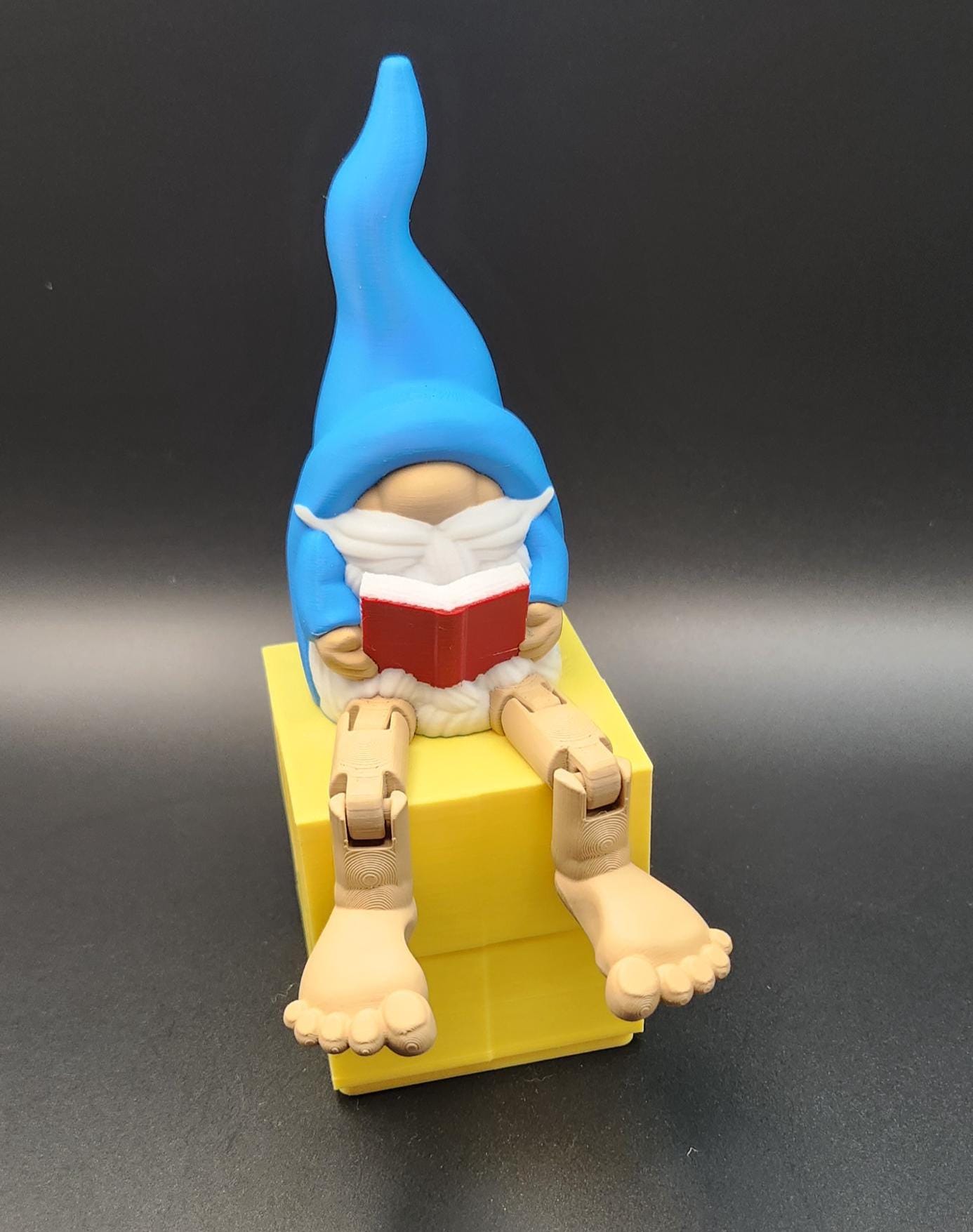Book lover gnome ornament shelf buddy with blue hat reading a red book sitting on a yellow block
