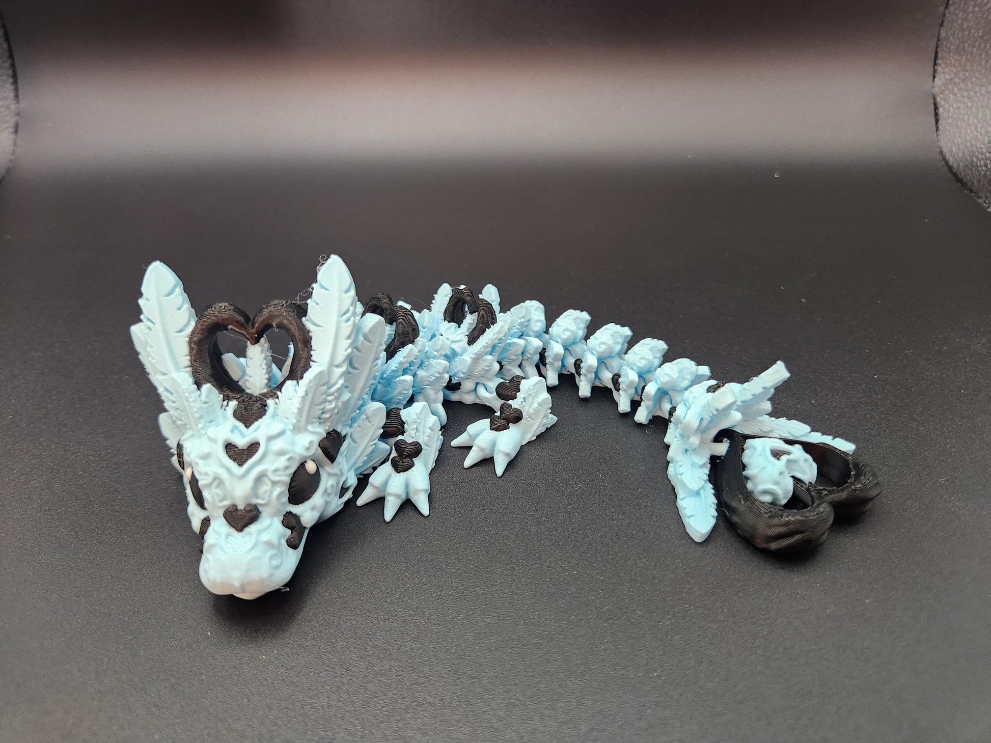 Cute flexy heart dragon figurine in blue and brown with heart details and flexible body on black background