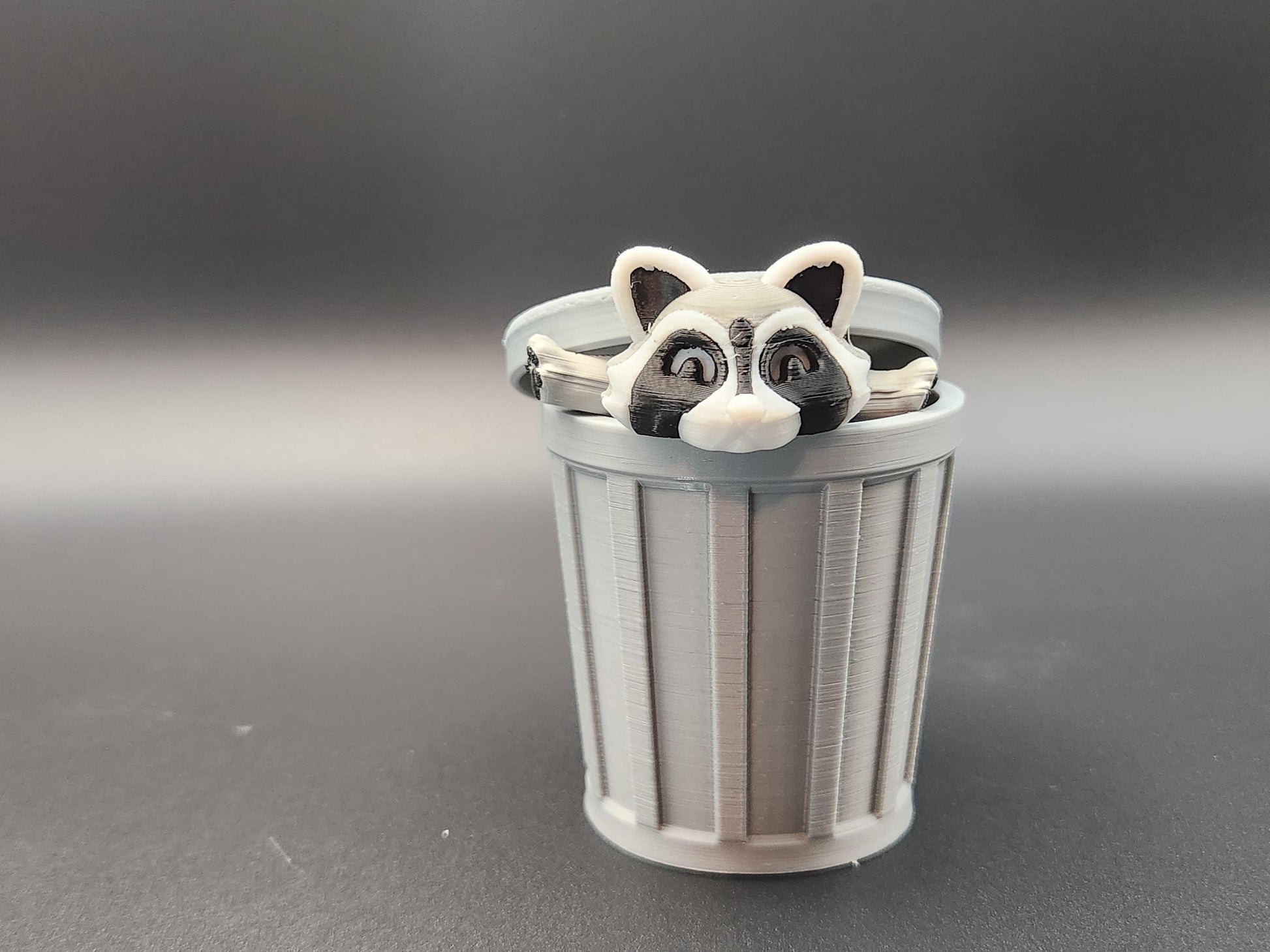 Articulated raccoon fidget figure peeking out of a gray trash can toy from Etsy