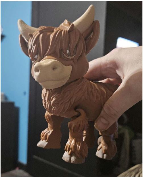 Hand holding a cute brown Highland cow decor figurine with detailed fur and large horns