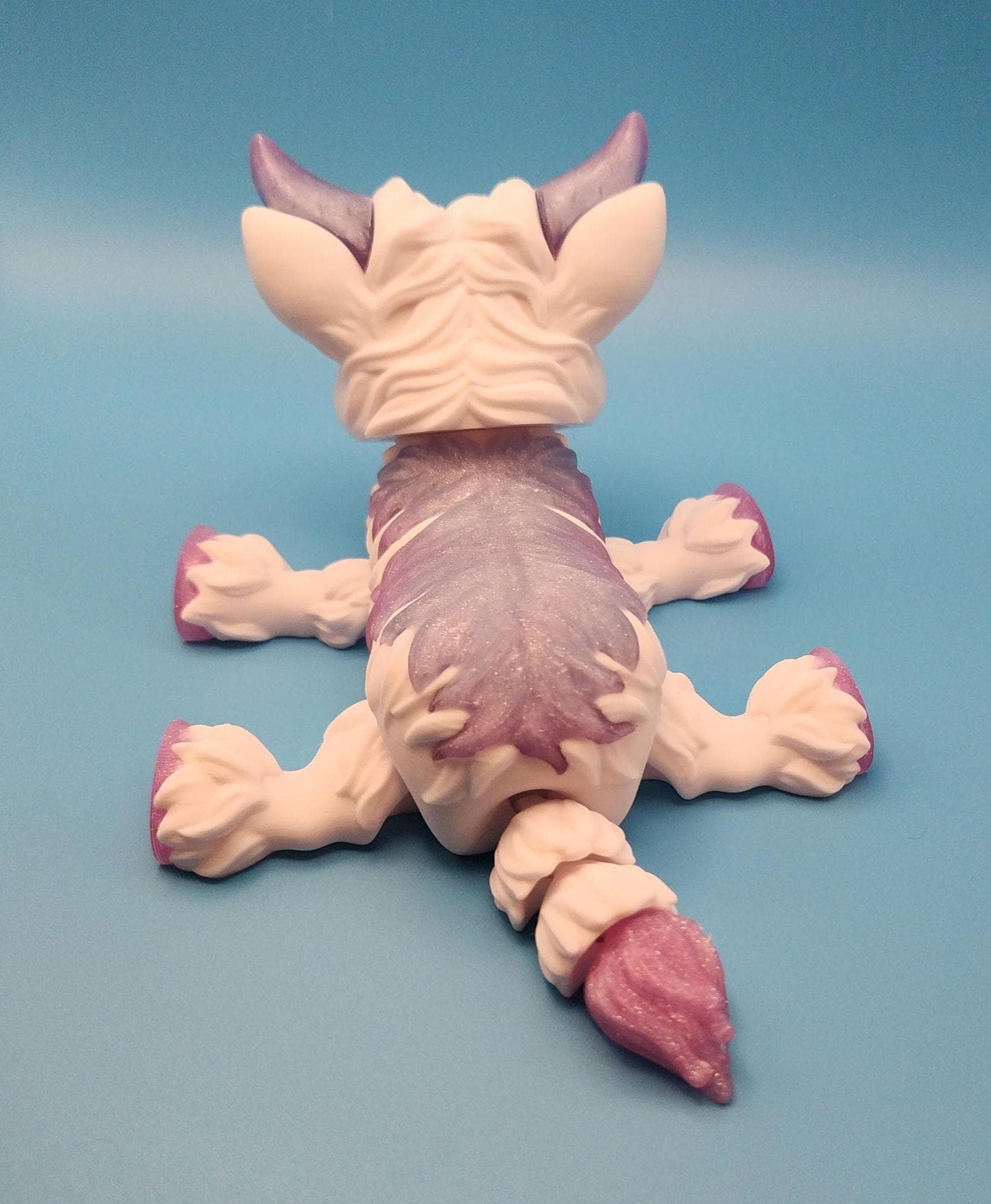 Purple and white Highland cow decor figurine lying down with detailed textured fur on blue background