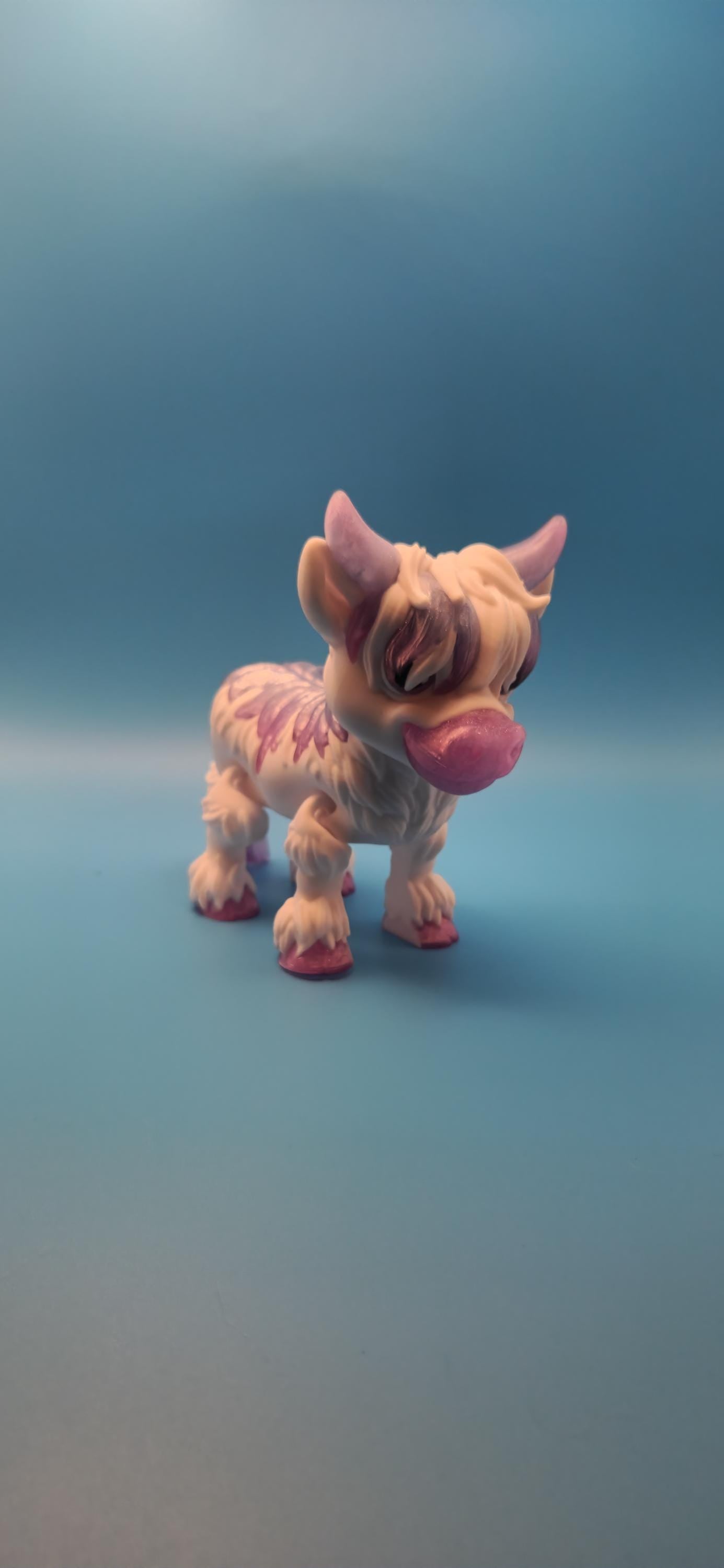Cute small figurine of a fluffy Highland cow decor with pink accents on a blue background