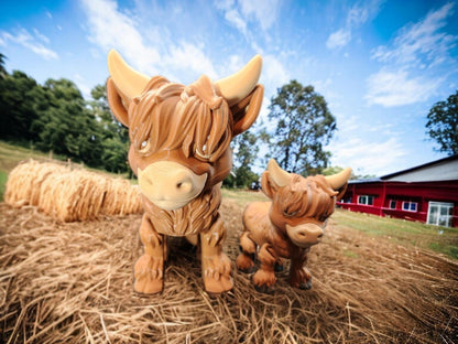 Cute ceramic Highland cow decor figurines displayed outdoors on straw near a red barn
