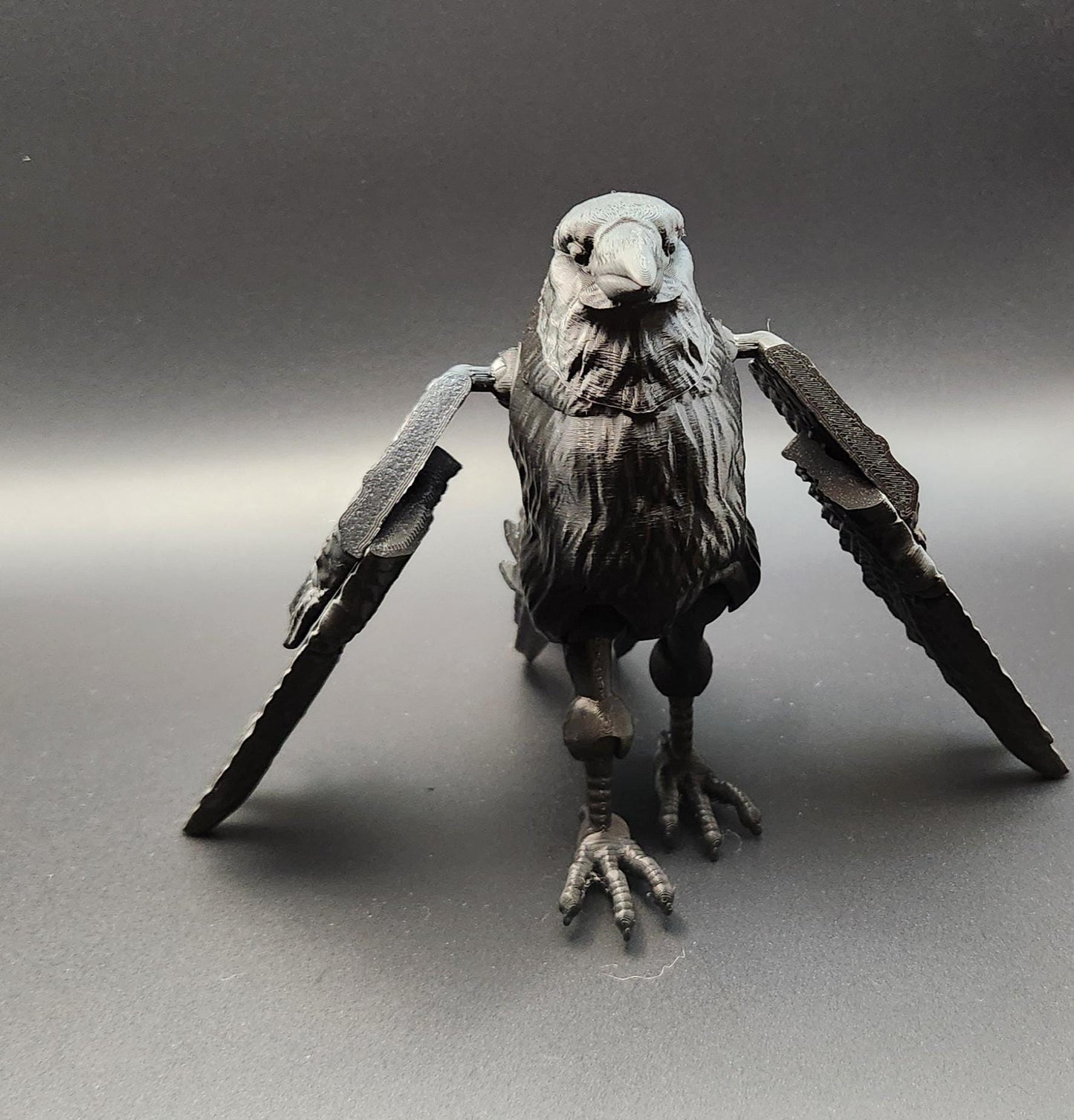 Black detailed articulated raven figurine with spread wings on a gray background
