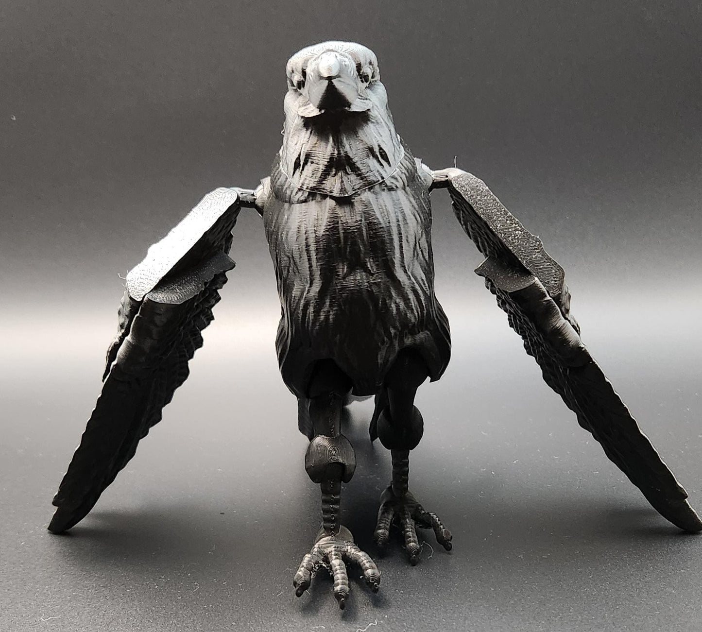 Black articulated raven figurine with detailed feathers and wings spread open on gray background