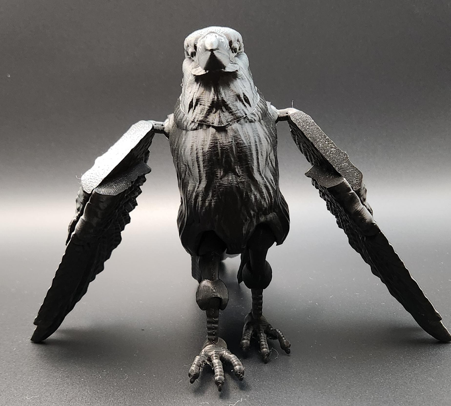 Black articulated raven figurine with detailed feathers and wings spread open on gray background